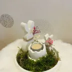 Dekoriertes Osternest mit zwei Hasen und einem Ei mit Kerze auf Grundplatte